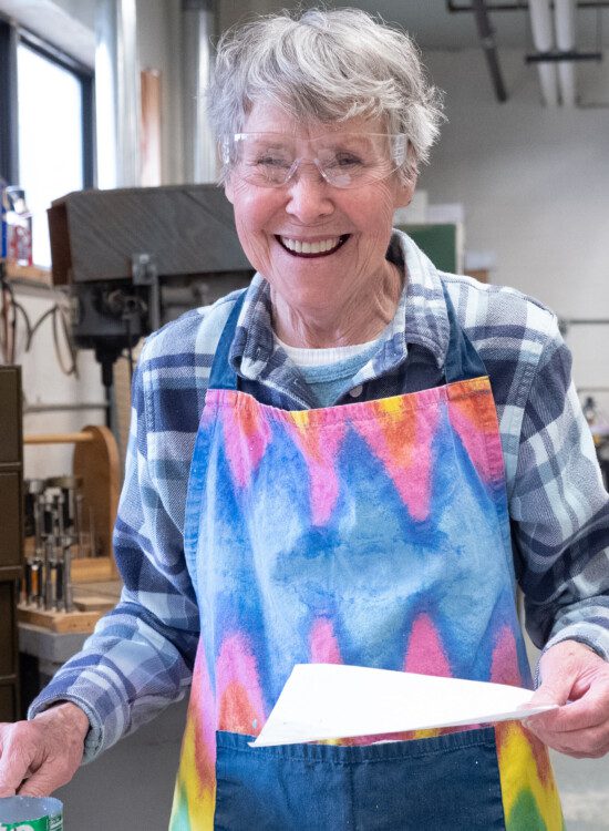 senior woman wearing protective glasses smiles during woodworking project